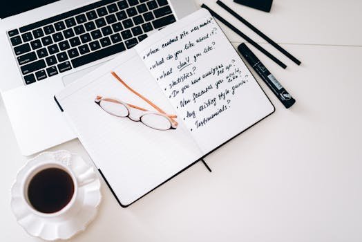 A stylish workspace featuring a laptop, notebook with notes, glasses, and a coffee cup.